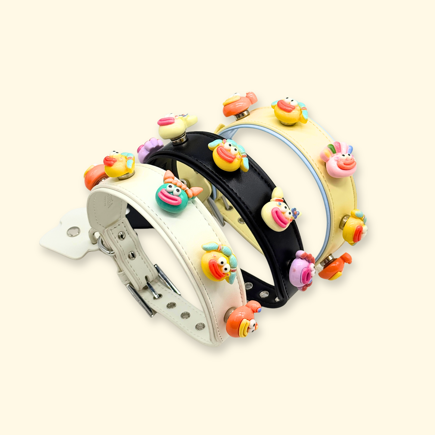 Three angled dog collars in pastel cream black and yellow featuring interchangeable emoji charms for pet fashion customization