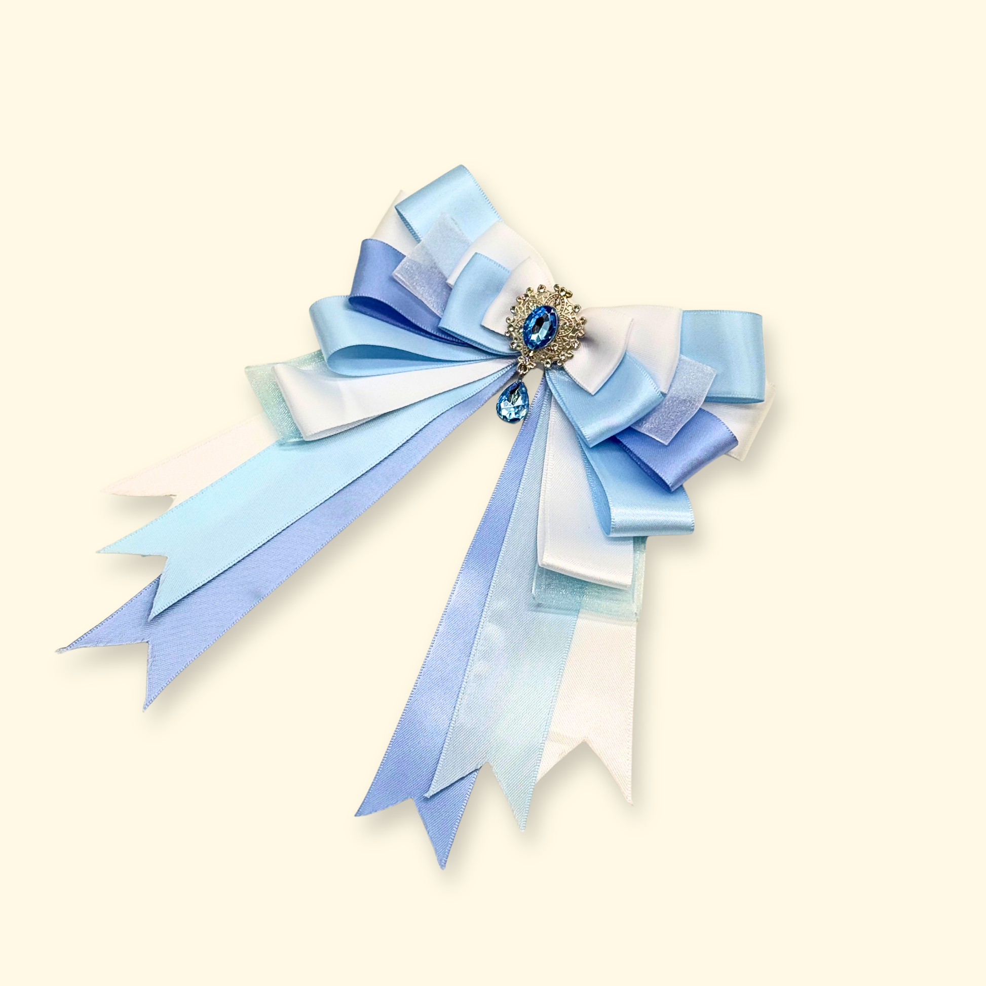 Close-up of Petiria blue diamond bow collar charm on beige background, highlighting ribbon layers and sparkling diamond centerpiece