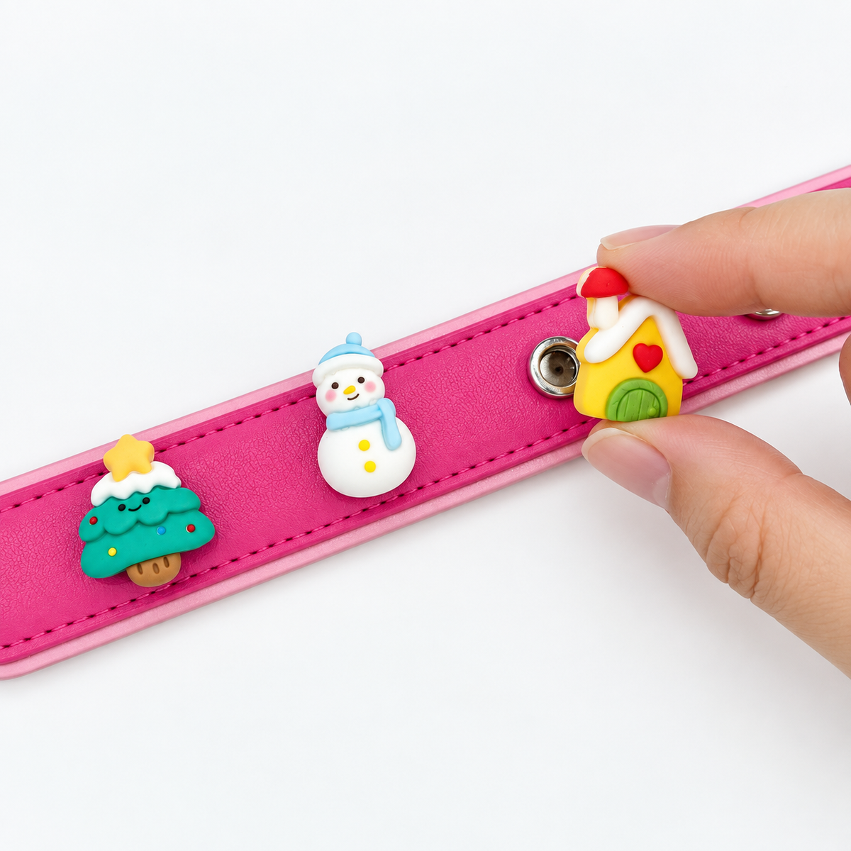 Little Christmas house charm being snapped onto a pink Petiria interchangeable dog collar with snowman and tree charms