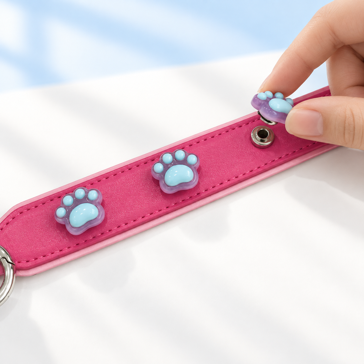 Blue paw print dog collar charm being snapped onto a pink Petiria interchangeable charm collar