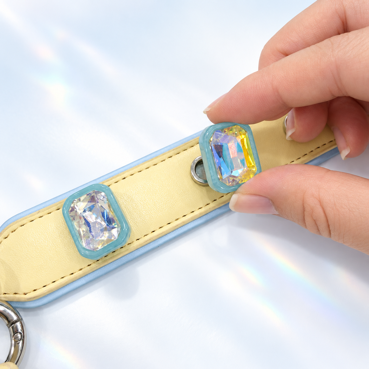 Hand attaching an interchangeable Blue Aurora crystal dog collar charm to a yellow PETIRIA collar