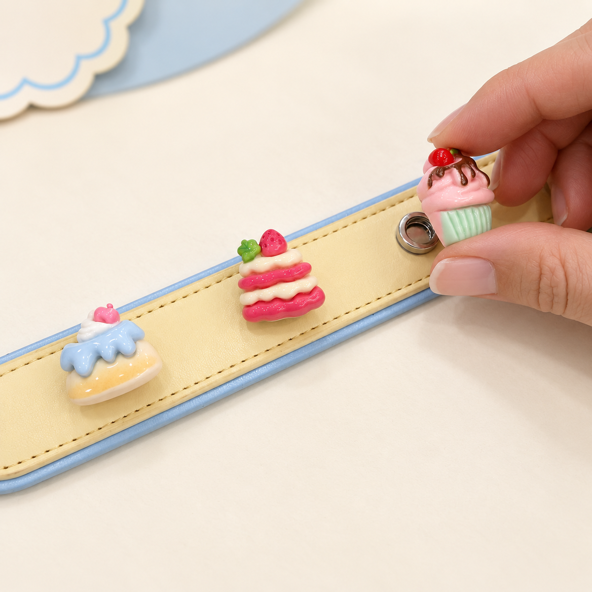 Hand attaching an interchangeable cake dog collar charm to a yellow PETIRIA collar