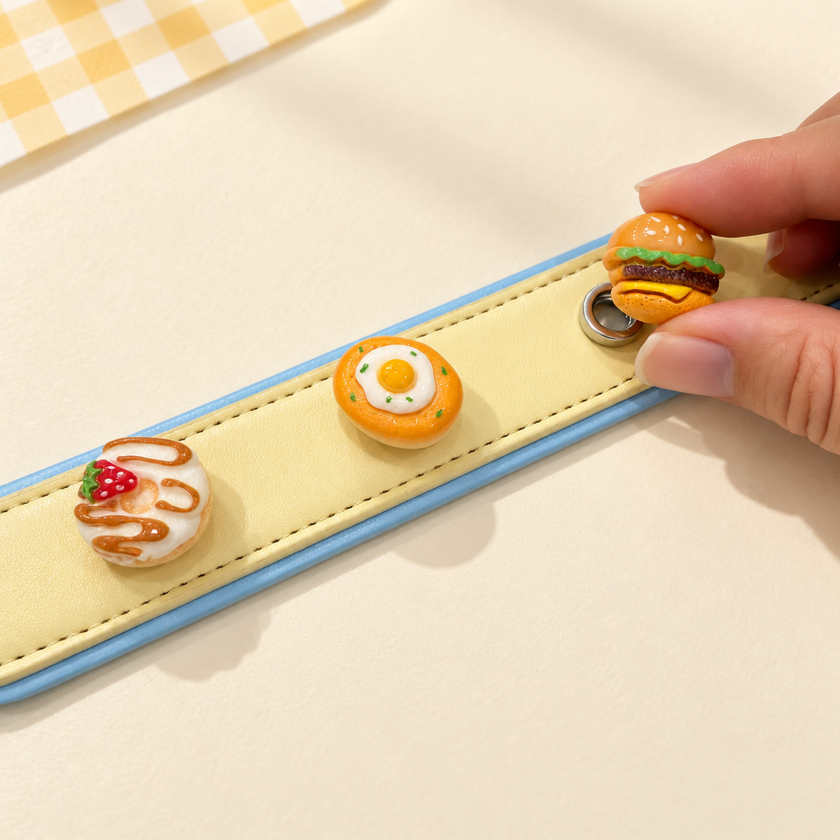 Hand attaching a burger dog collar charm to a yellow PETIRIA collar styled with cute food charms