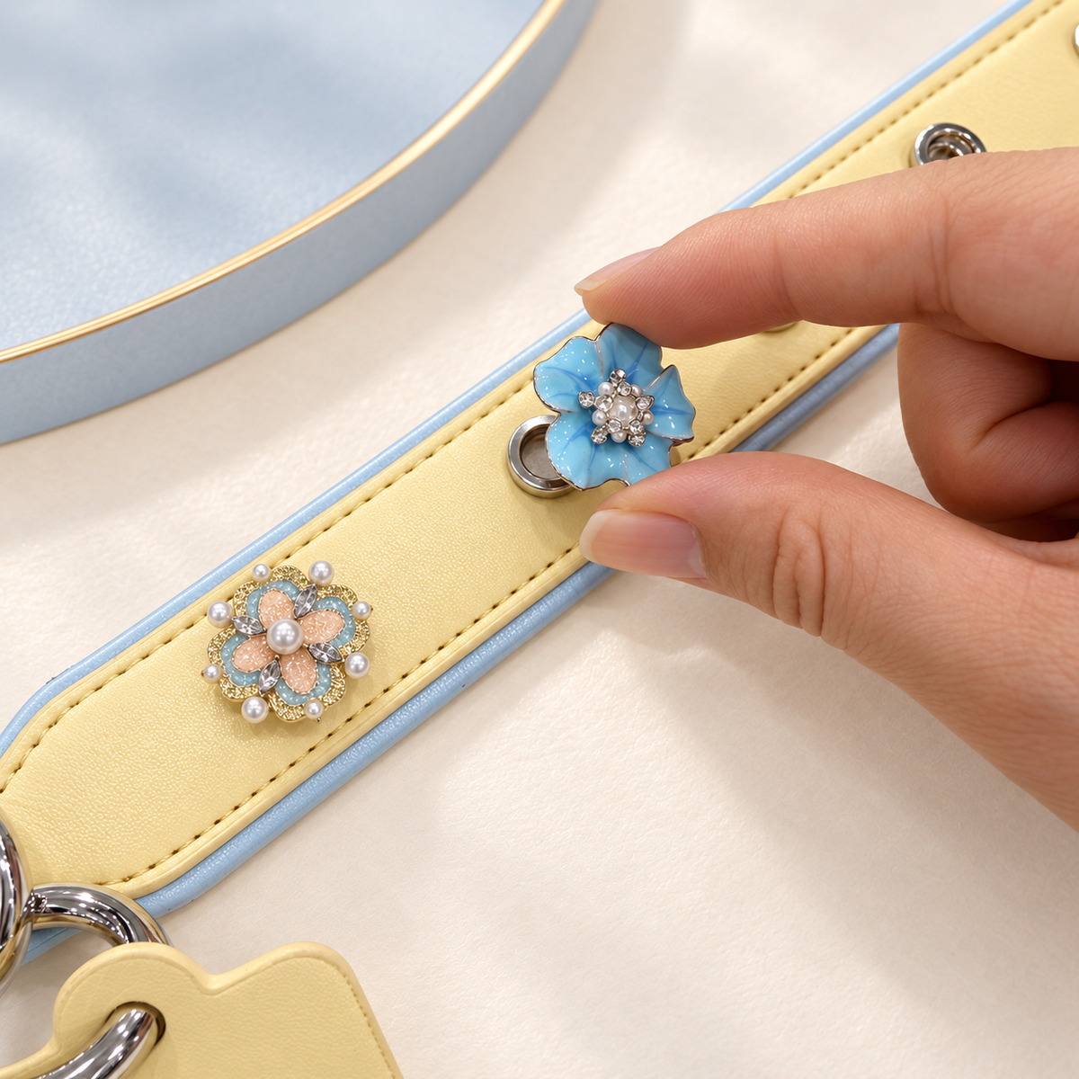 Hand attaching a blue flower dog collar charm to a yellow PETIRIA collar