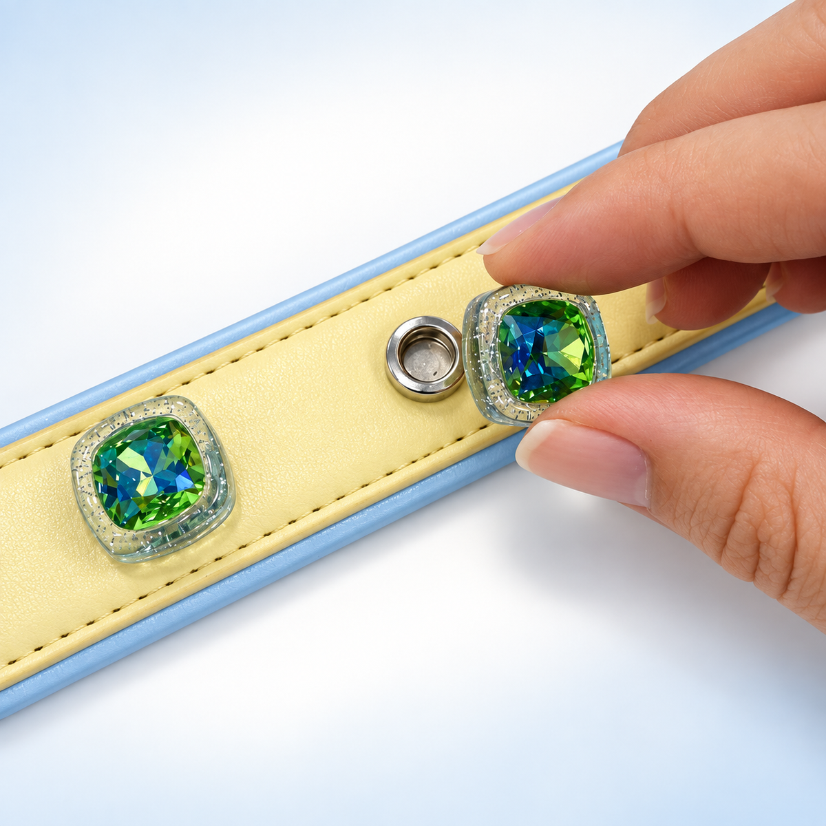 Hand attaching an interchangeable green gem dog collar charm with gold-tone frame to a yellow PETIRIA collar
