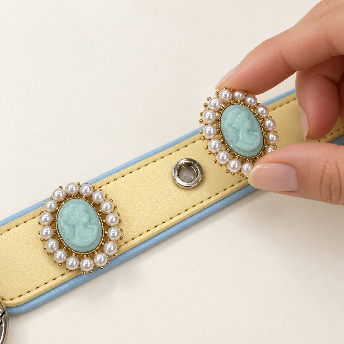 Hand attaching a blue pearl cameo dog collar charm to a yellow PETIRIA collar