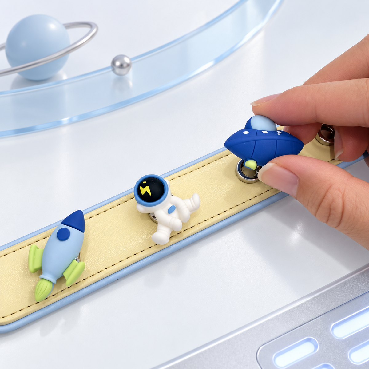 Hand attaching a Cosmic UFO dog collar charm to a yellow PETIRIA collar with astronaut and rocket charms