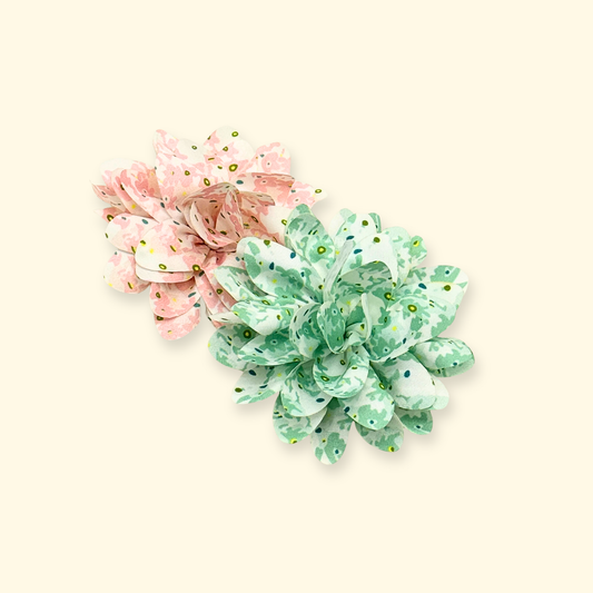 Top-down view of Petiria floral collar charms in pink and green, arranged on a soft beige background
